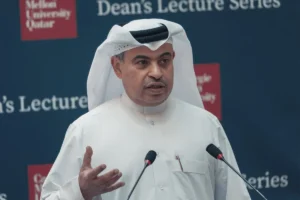 Man in white thobe delivering a speech at a Dean's Lecture Series event, with two microphones in front.