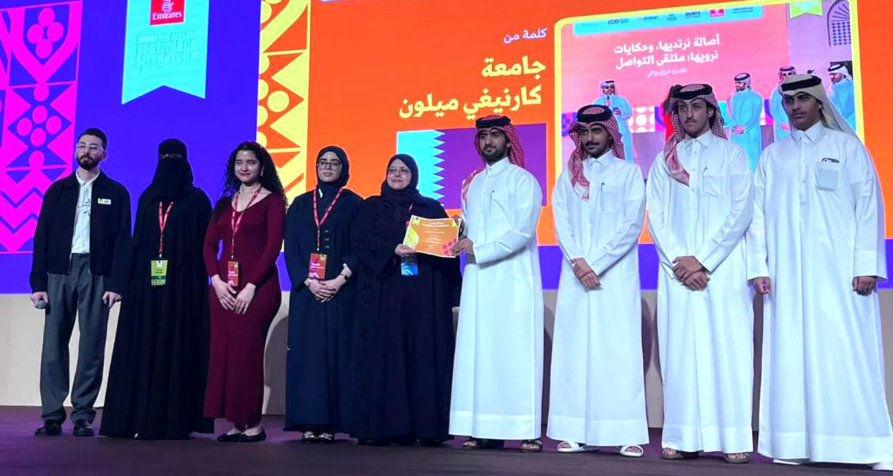 Group of people on a stage during an award ceremony, receiving a certificate, with a bright orange and purple backdrop behind them.